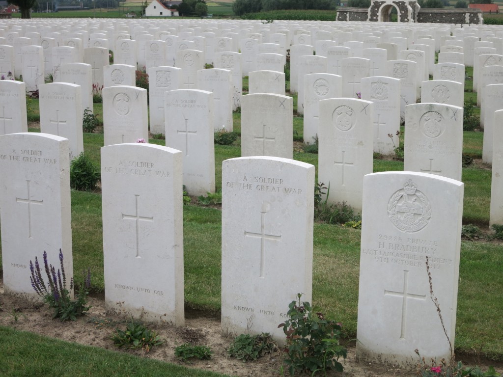 Belgium war graves in Tyne Cot cemeteray. Rows of simple white gravestones. Most have a large crosee in the center. Many have a military insignia of some sort carved above that. Many just say "A soldier of the Great War" in place of the insignia and then, below the cross, the words "Known unto God." The nearest stone in the picture has a name: It reads "29886 Private H. Bradbury East Lancashire Regiment 9th October 1917" 