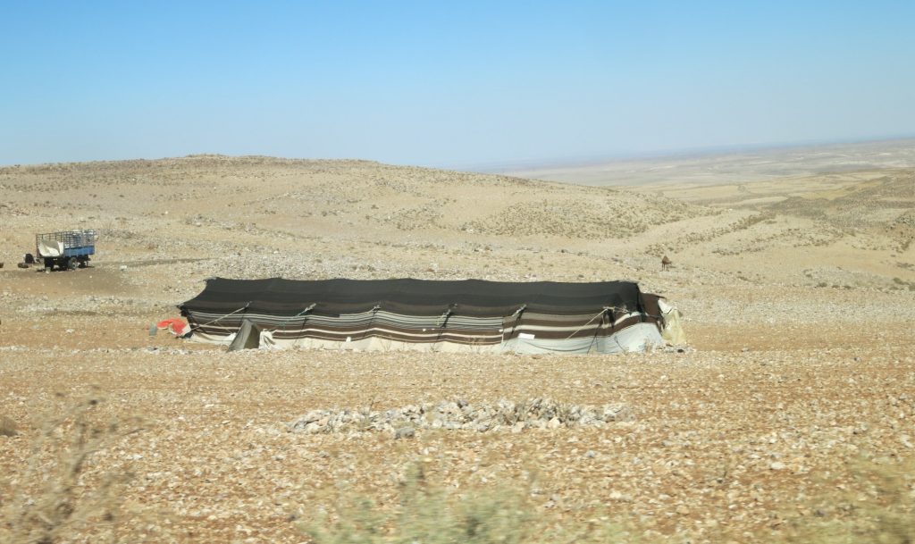 A brown plain with a long low tent in the middle, as seen from our Jordanian taxi.