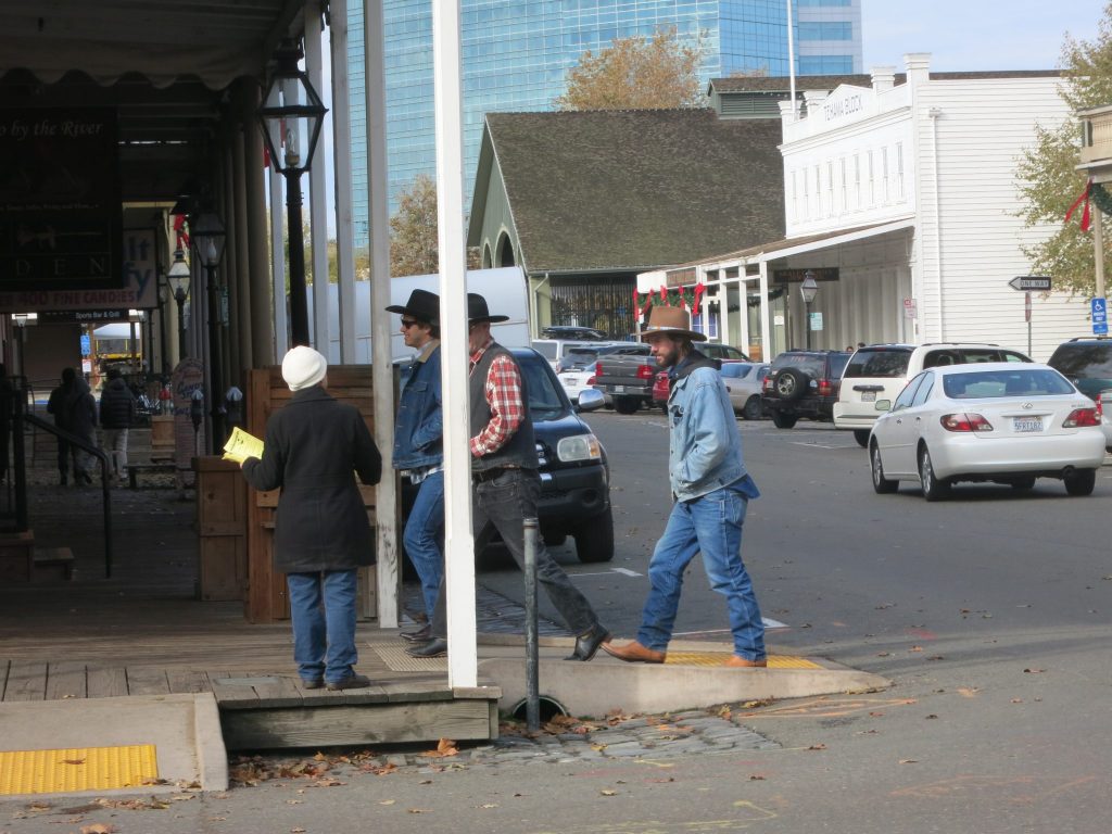 Three men in cowboy hats and cowboy boots have just cross the street from right to left. In the photo they're just entering the covered sidewalk. 