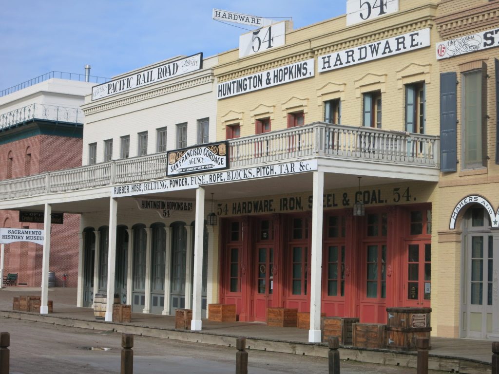 Two buildings, 2 stories tall each. Across both buildings a large balcony over the sidewalk, supported on pillars. Signs on the buidings read, from left to right, Pacific Rail Road, Huntington & Hopkins, Hardware. Smaller signs on the railing of the balcony read San Francisco Cordage Agency and Rubber Hose, Belting, Powder, Fuse, Rope, Blocks, Pitch, tar, &c.
A stop on our weekend trip from San Francisco.