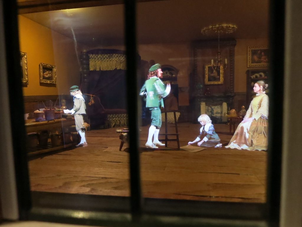 The painter wears knickers and a beret, while a woman poses with a child on the floor in front of her. At the Canal House Museum in Amsterdam.