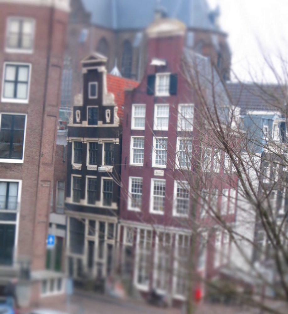 two row houses of brown brick, with step gables and lots of windows. The one on the left leans a little out over the street.