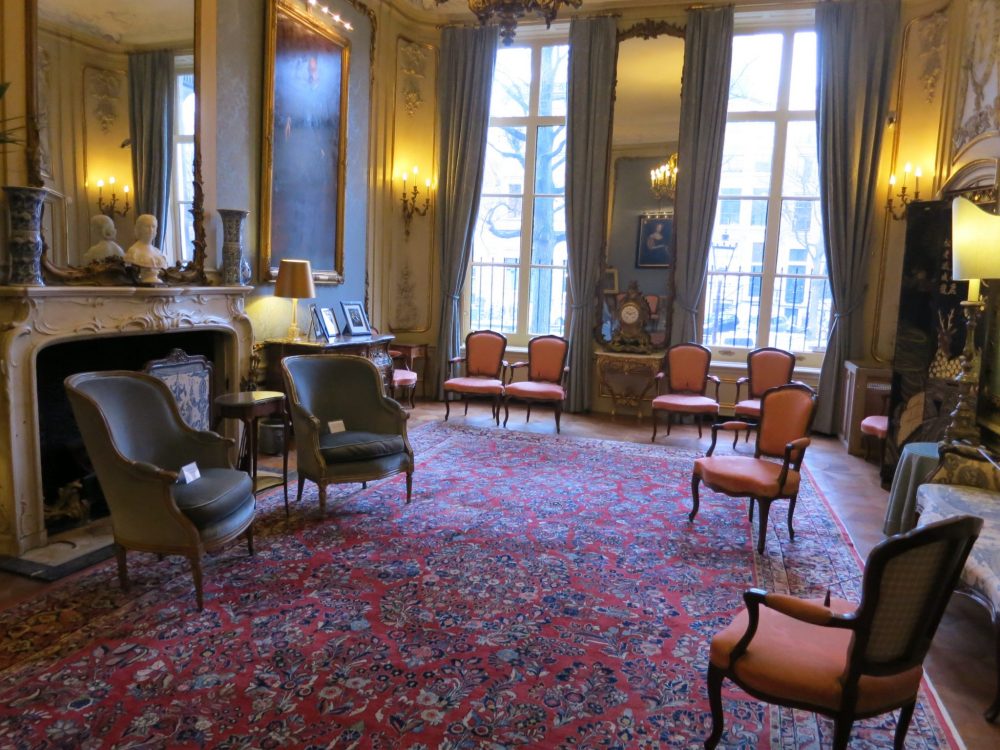 An elegant drawing room with dark red flowered carpet and a scattering of chairs at the Museum van Loon.