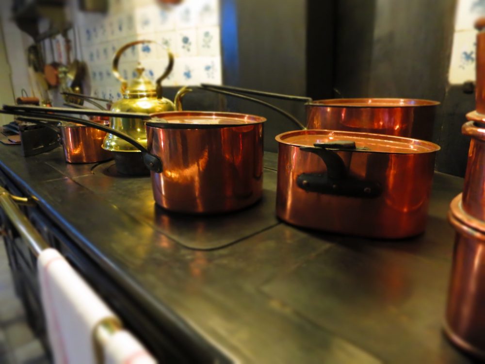 The cast iron stove with several shiny copper pots on it.