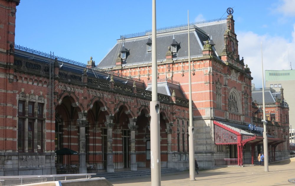 view of Groningen train station: red brick with stone details around windows and roofline. Mansard roof. 