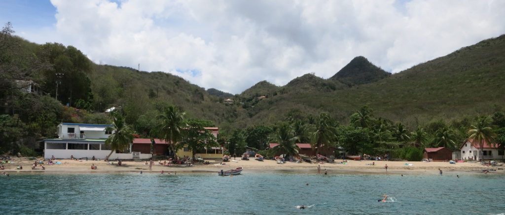 a view of the beach with a few small buildings and palm trees, with mountains behind them