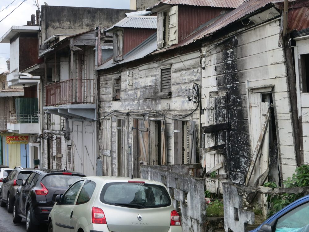 view of a row of wooden houses in Guadeloupe, in very bad condition, looking like there might have been a fire.