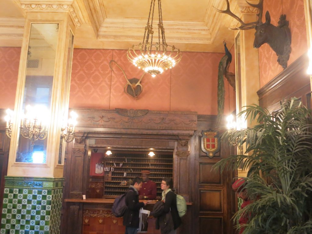 the reception area of the Jane Hotel showing stuffed animal heads and a stuffed peacock on the wall, and an employee in bellhop's uniform