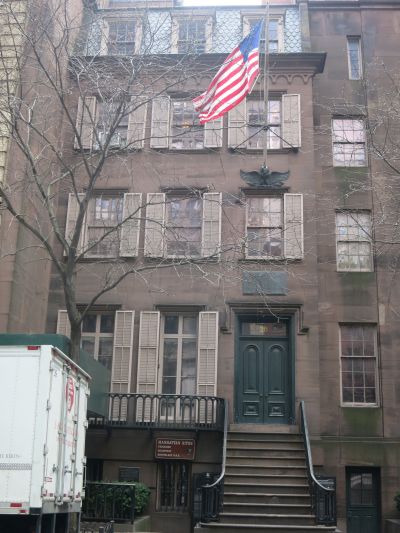 A tall narrow rowhouse of brick with a big American flag.