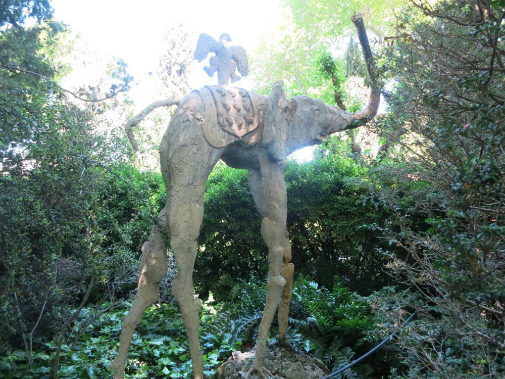 Surrounded by greenery in the garden of the Gala Dali castle, this elephant/insect is perhaps 10 feet tall and has a bird of some sort sitting on its back.