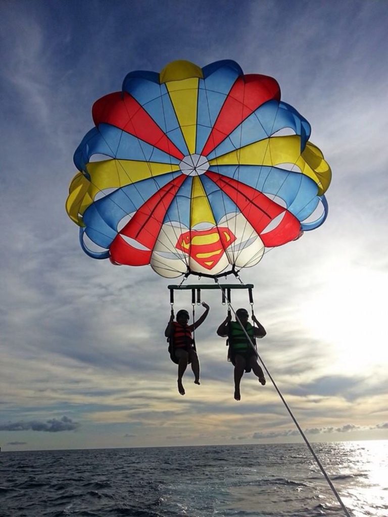 two people strapped under a parachute, parasailing