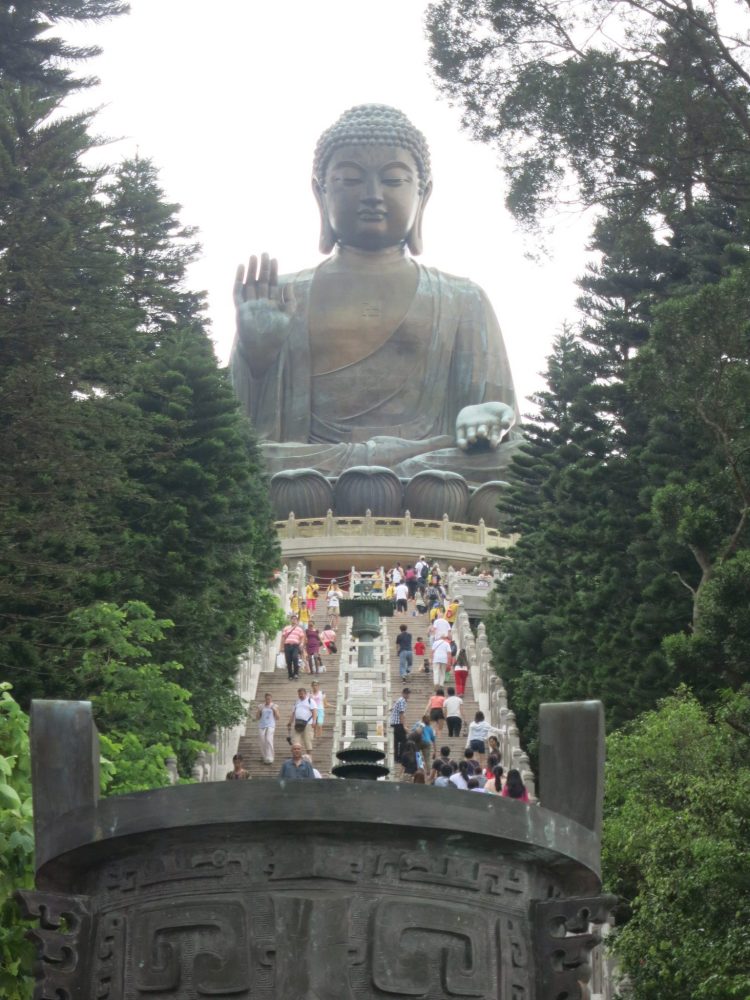 view up the stairs with the Big Buddha at the top. The people on the long stairway are not even as tall as the Buddha's fingers. The Buddha sits cross-legged, with one hand flat, palm turned up, and one hand raised, palm turned forward. His eyes are shut.