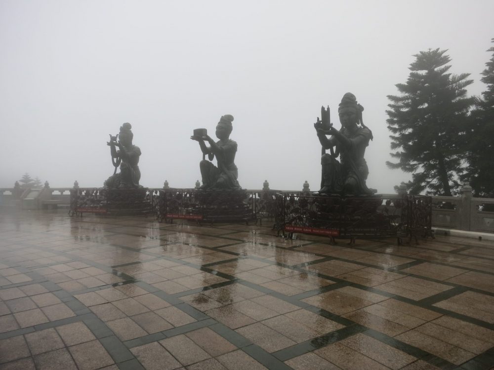 Three of the Deva statues, making offerings to the Buddha above. It was raining hard when the photo was taken, so the three statues are rather fuzzy. Each kneels and holds something up in both hands as an offering. 