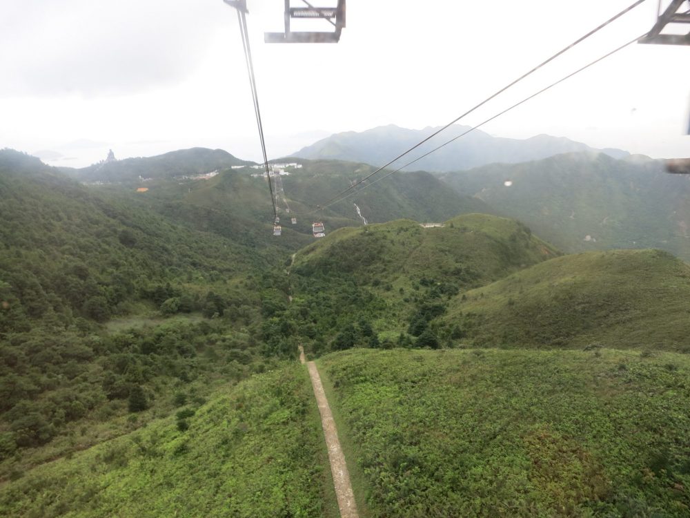 a view over green hills from the cable car, with the Big Buddha on a hill in the distance