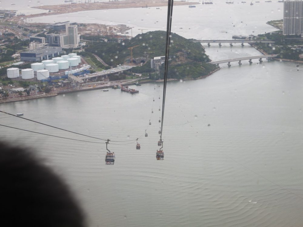 view down showing the cables stretching over the bay, on the way down from the Big Buddha. A number of cars hang from the cable at equal distances from each other.