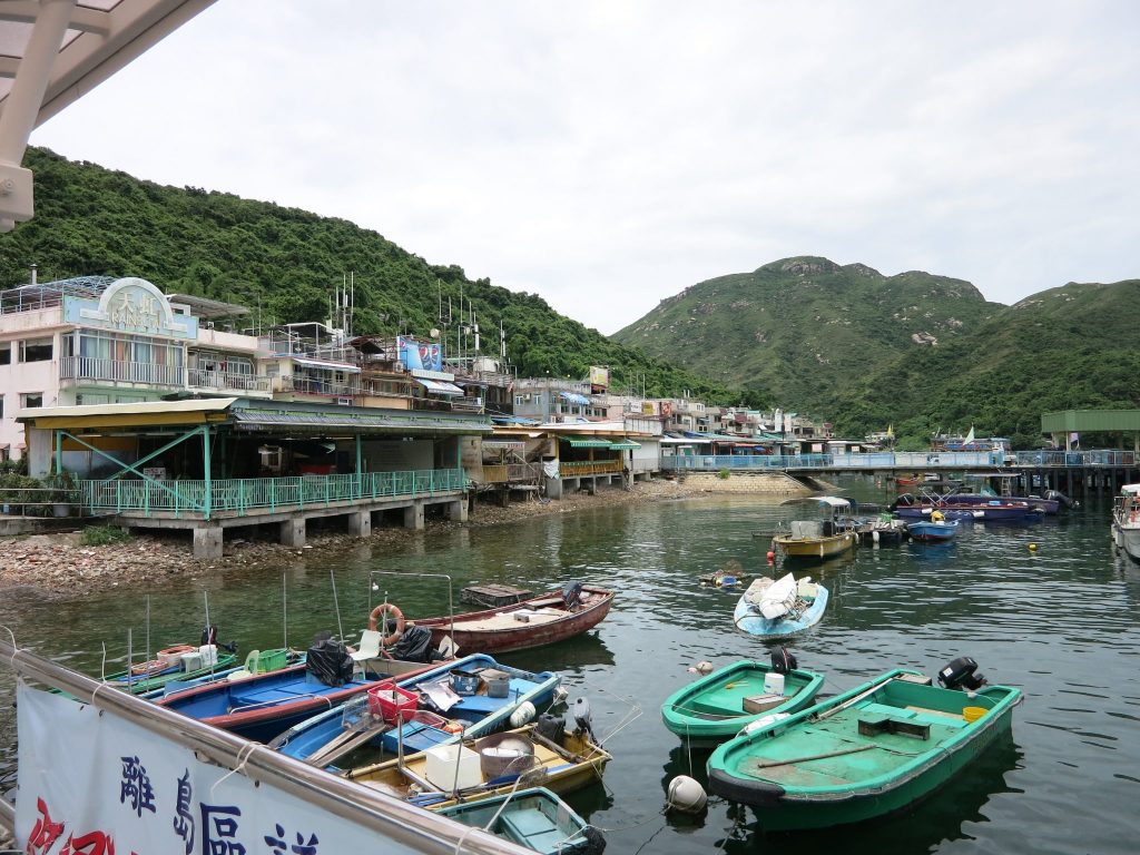 small fishing boats in the foreground, houses partly on stilts in the background, with large balconies: on Lamma Island