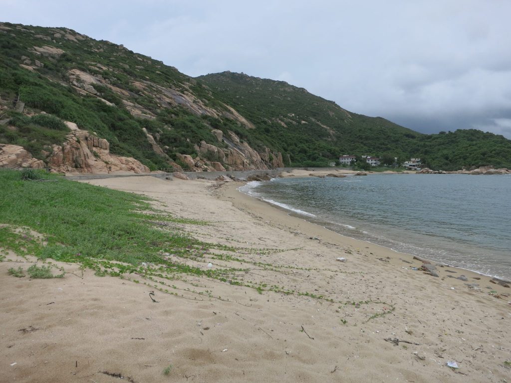 a stretch of empty beach, with a small cluster of buildings visible in the distance, on Lamma Island