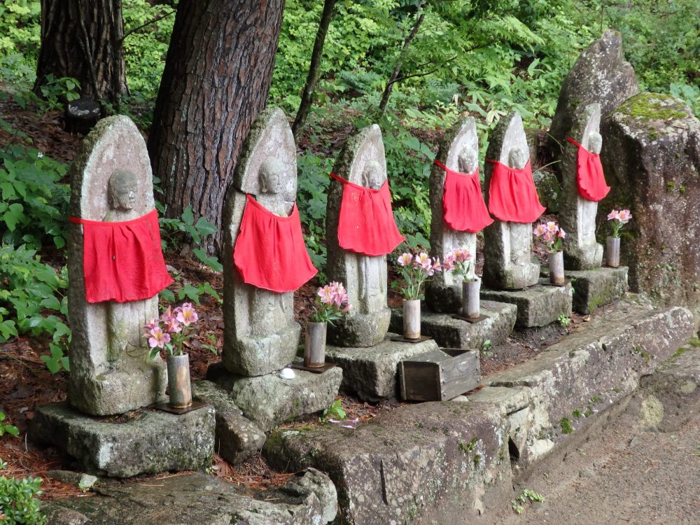 a row of six stone statues, each wearing a red cloth as a sort of bib, in the Hida Folk Village in Takayama, Japan