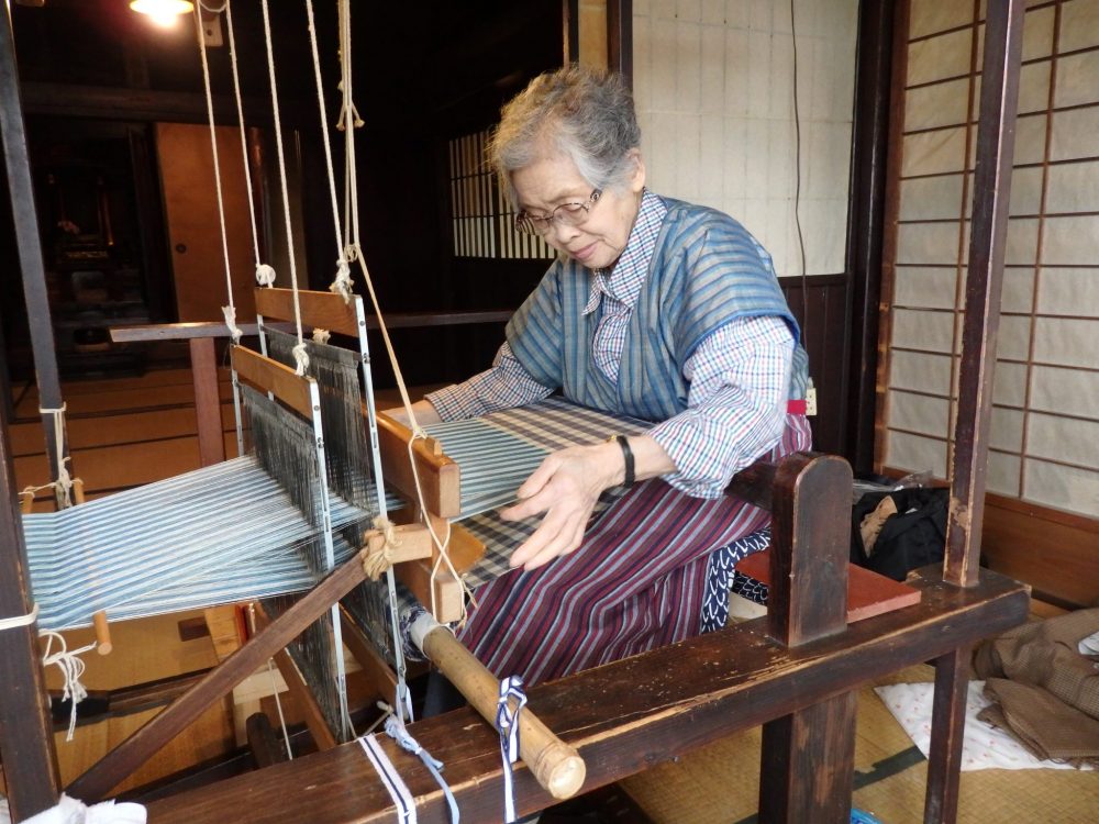 A woman sitting and busy operating an old-fashioned loom. 