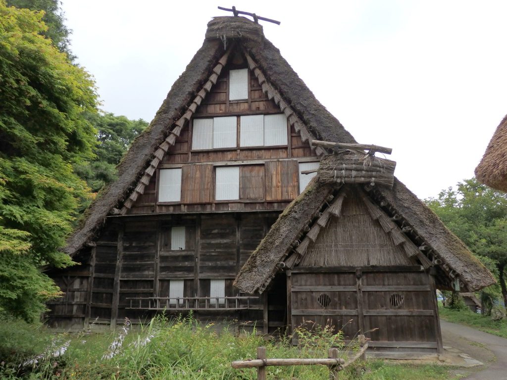 A high, thatched peaked roof, wooden front, with sliding shutters over the windows. 