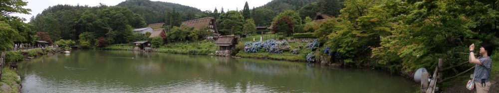 a pond, with a few houses and a mill next to it, at Hida Folk Village