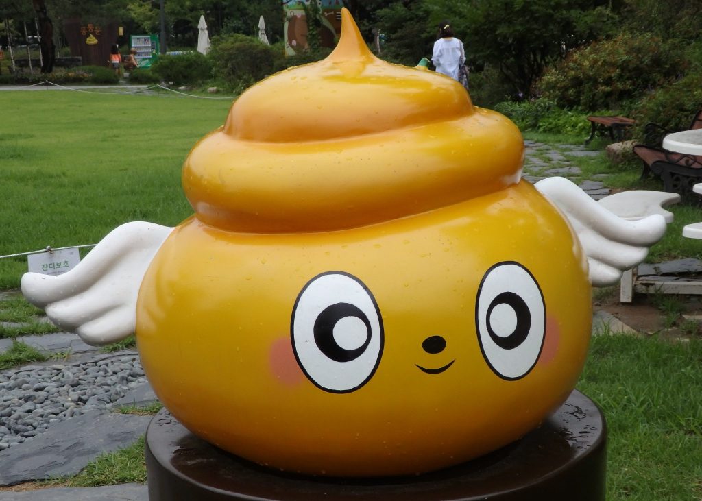 The figure is yellow, and turd-shaped, but has big eyes painted on and two small white wings peeking out from behind.
