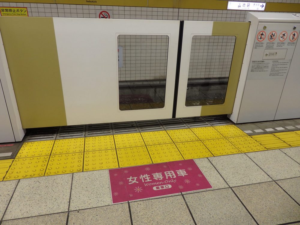 sign on the floor marking a women-only car during rush hour: red sign, printed in Japanese and English