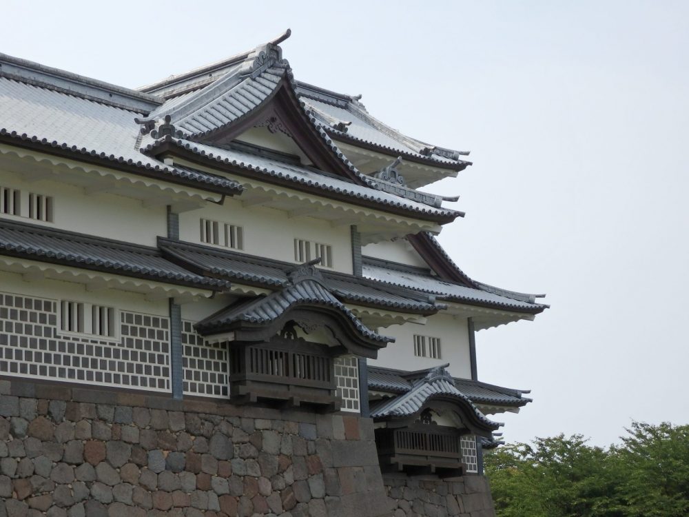 The building is primarily white, with some stone bricks on the ground floor and typical Japanese rooflines that curve. The building stands on a stone wall foundation.