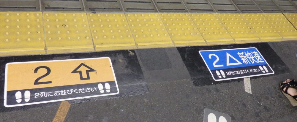 signs on the floor of the platform indicate where to wait. On the left, a yellow sign with an upward arrow and the number 2. On the right, a blue sign with a triangle and the number 2.