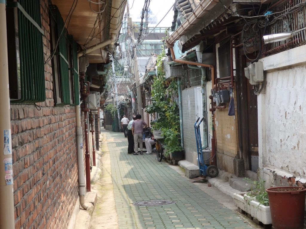 a street in Ikseon Hanok Area: quite narrow, a tangle of wires overhead, a variety of different wall facades: brick and plaster mostly.