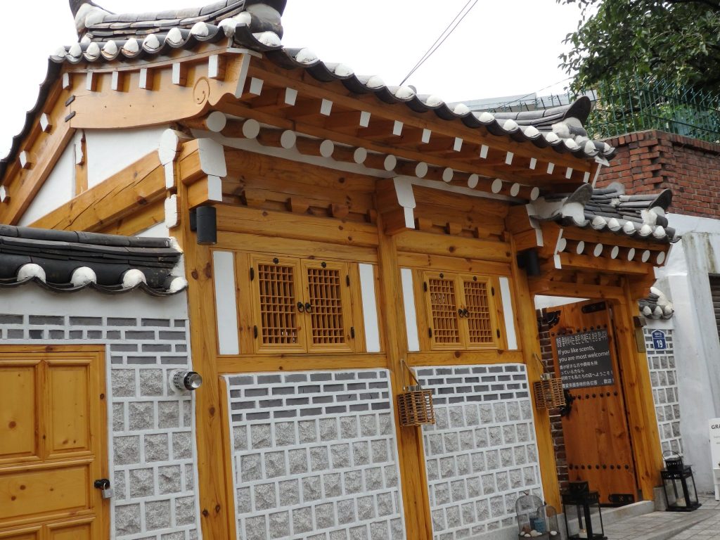 This hanok appears to be new, and houses a scent shop. The same design as the picture above: stone below, brick work above that, then wood framing white plaster and small windows and roof beams sticking out above, but these roof beams are a lighter wood.