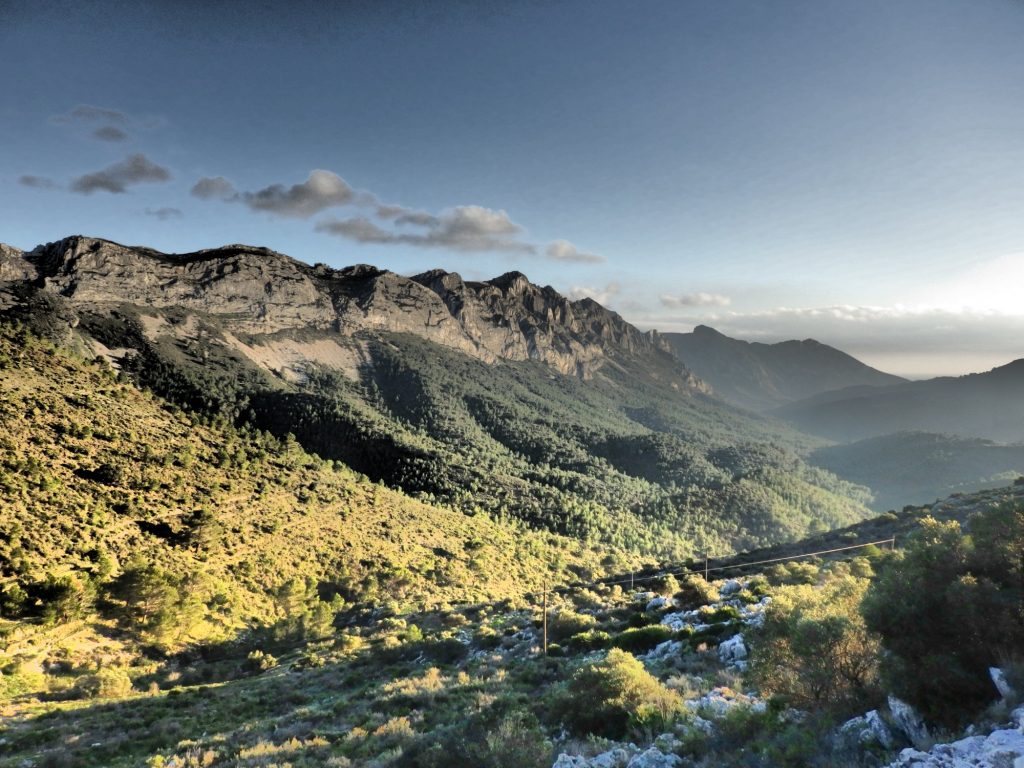 a beautiful Costa Blanca view over a valley. There are no buildings in sight. The valley is covered in low, scrubbly plants. On the other side is a ridge of exposed stone.