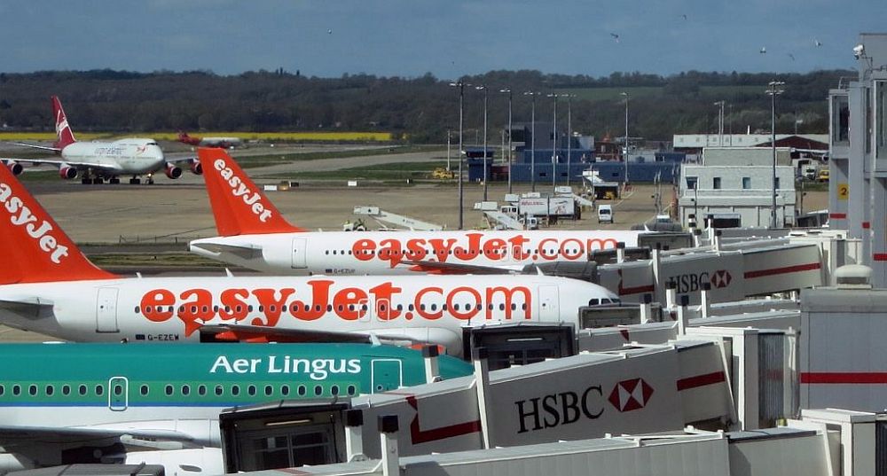 The jets are parked at a gate. Visible are two easyJet planes and an Aer Lingus plane. Behind them a 747 approaches from the runway.