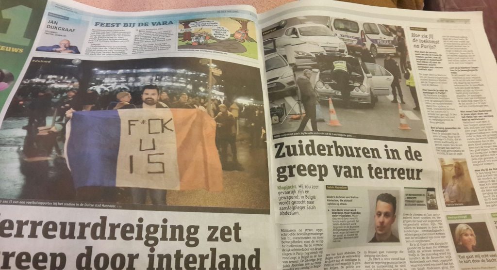 An open newspaper. Picture in the paper on the left has a man holding a French flag with the words F*CK U IS on it. 