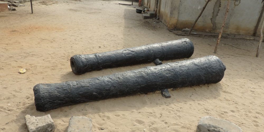 two antique cannons in Badagry, Nigeria, just lying on a sandy piece of ground.
