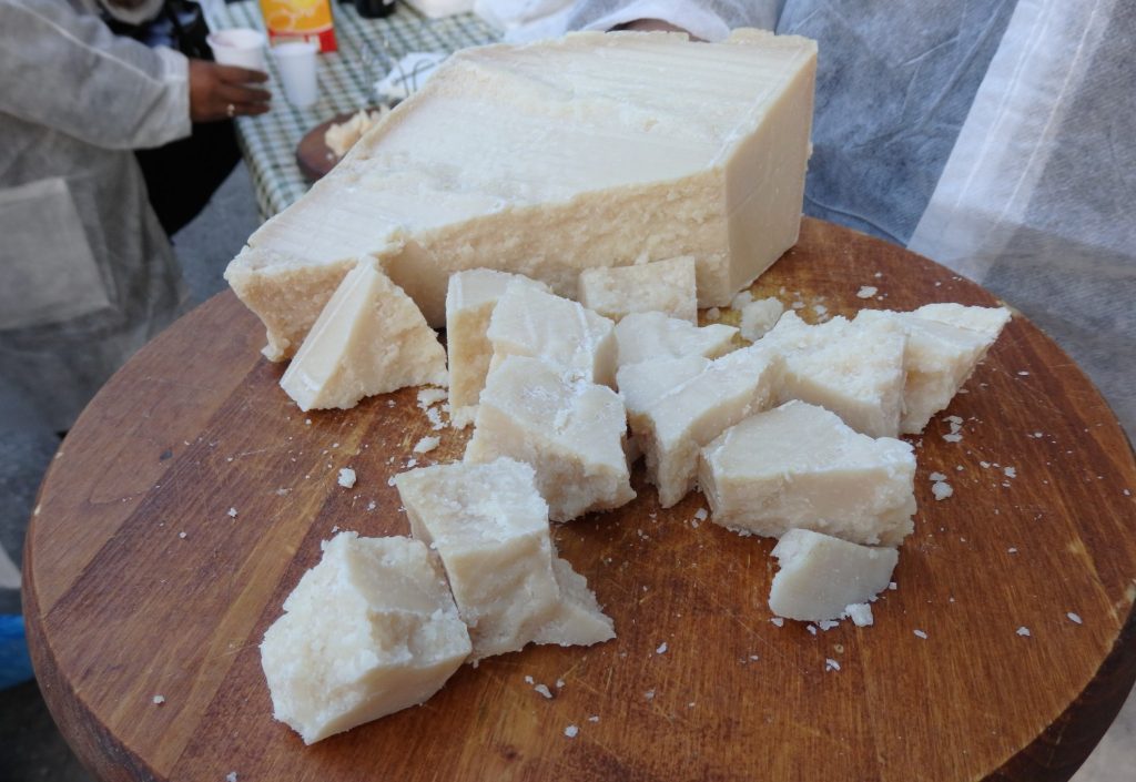 A large chunk of cheese on a wooden board, with smaller, crumbly looking chunks next to it. 
