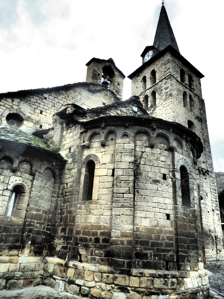 Stone church with simple details around the windows (romanesque arches) and rooflines. A square spire with pointed roof.