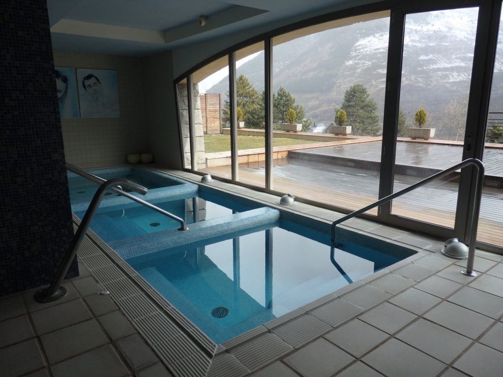 a spa with a view, in Vielha, Val d'Aran, Spain: three square pools set into the floor next to big full-length windows looking out on mountains.