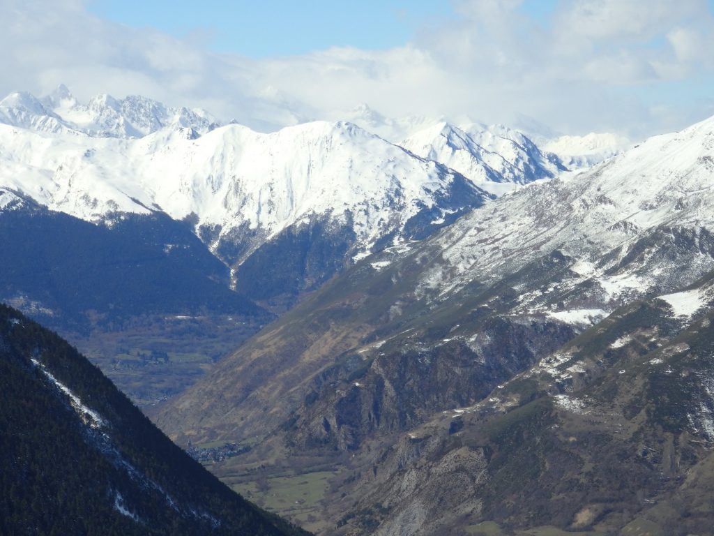 A big view over a deep valley with snow-capped mountains across the background.