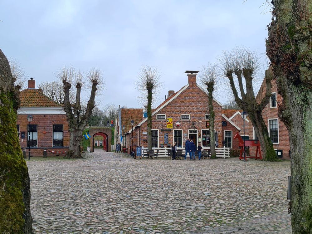 A large cobbled expanse of plaza, with small brick houses on the far end and trees around the edge of the plaza.