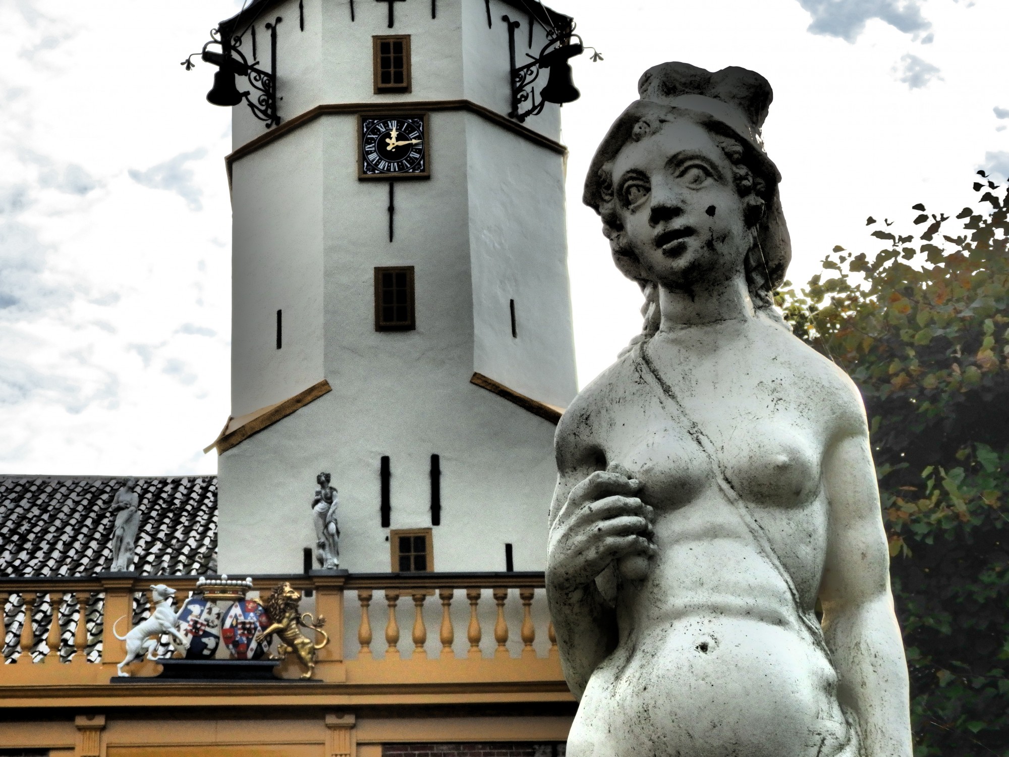 The statue is a naked female, slumping a bit and oddly proportioned. behind it, the tower is visible: white and six-sided, with a clock partway up and a couple of bells suspended outside it. The family cress has a dog on one side and a lion on the other.