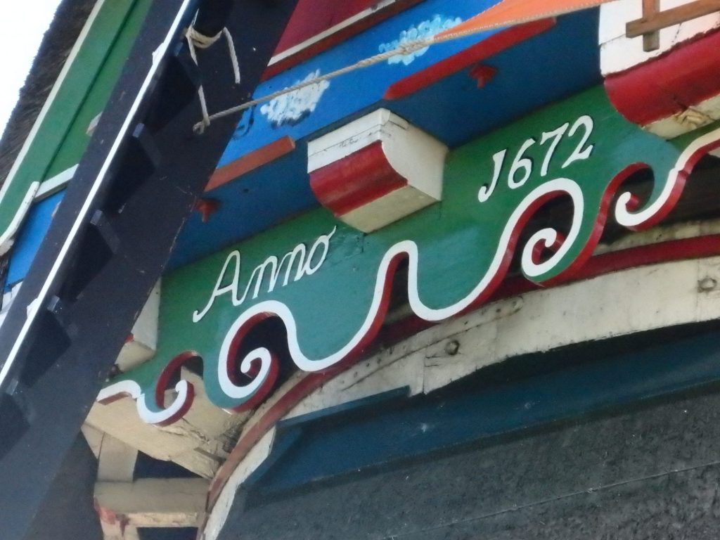 The woodwork is painted bright green, red, blue and white, with simple curles, like upside down waves, along the edge. The words "Anno 1672" are painted in white on a green background.