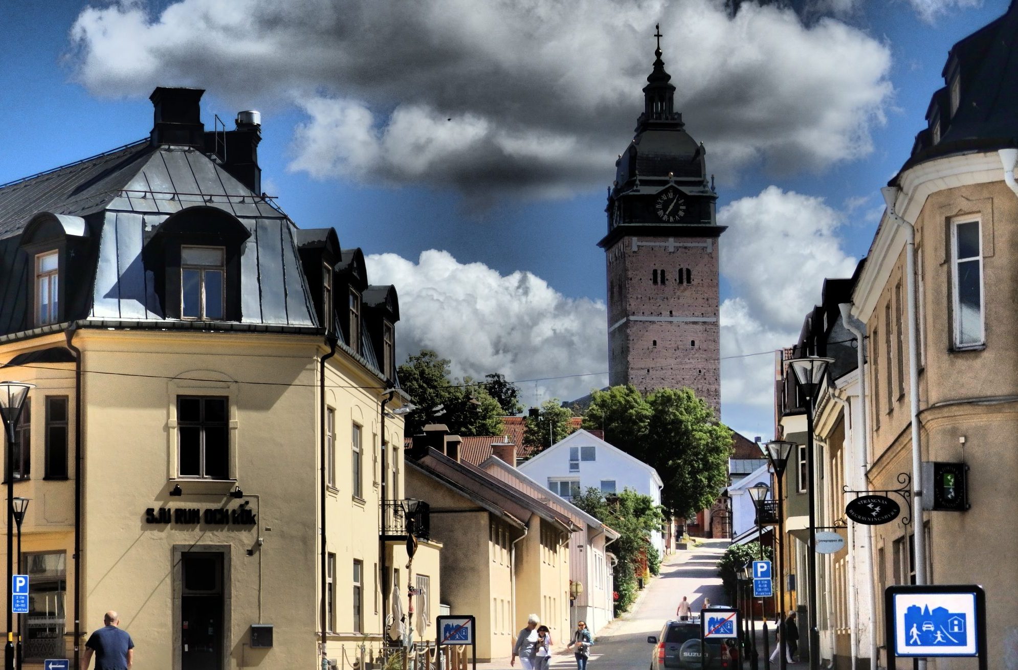 Looking down a small-town street toward a very tall square tower.