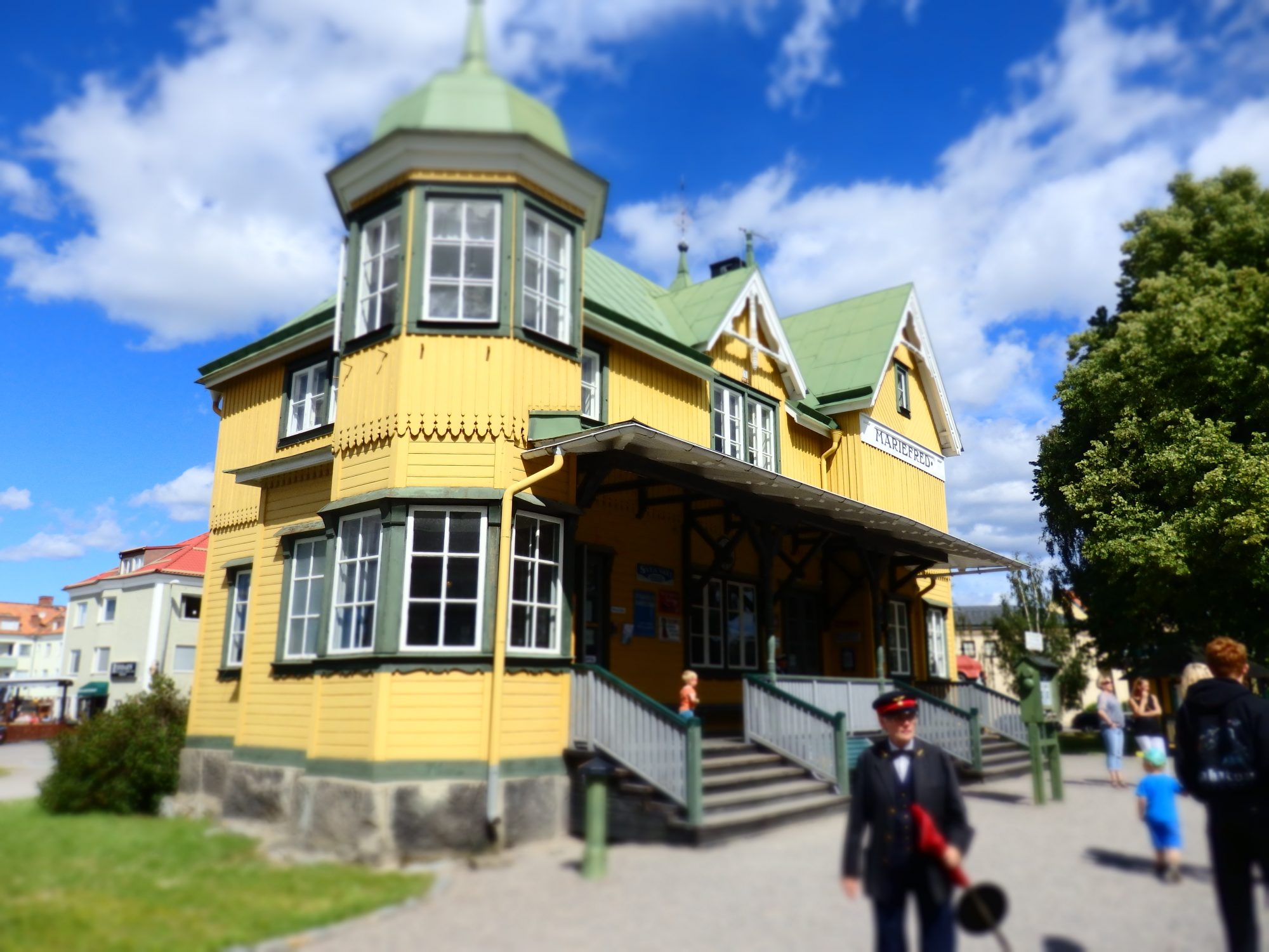 A yellow-painted victorian-style building, with a conductor standing in front.