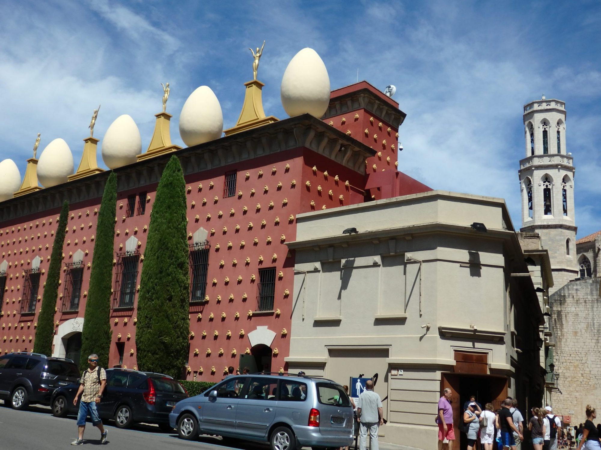 The outside of the building is dark red, with gold-colored bumps (actually a fat human figure from close up). Along the top is a row of large white eggs taller than a person. Between the eggs are a series of statues on pedestals painted gold.