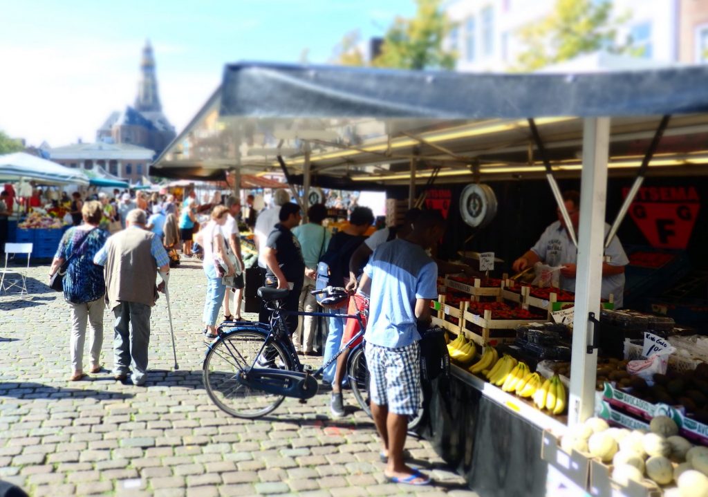 A market stall and people shopping, with other market stalls behind but blurrier.