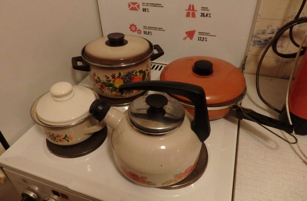 A stove with a teakettle, two pots and a saucepan on it. The pots are in a very 60's style, with flowers painted on the sides. One is an orange pan with a lid.