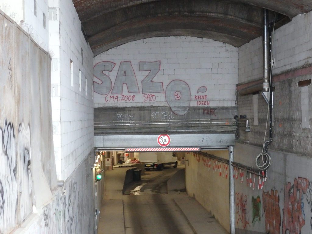 A view down a ramp into a parking garage, with a flat section of wall above the ramp where the word SAZo is painted.