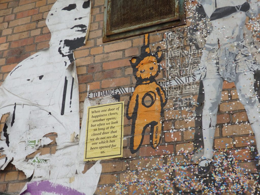 An image of a cartoonish teddy bear, much like Winnie the Pooh, but with a big round hole through its chest and it appears to hanging by a noose.