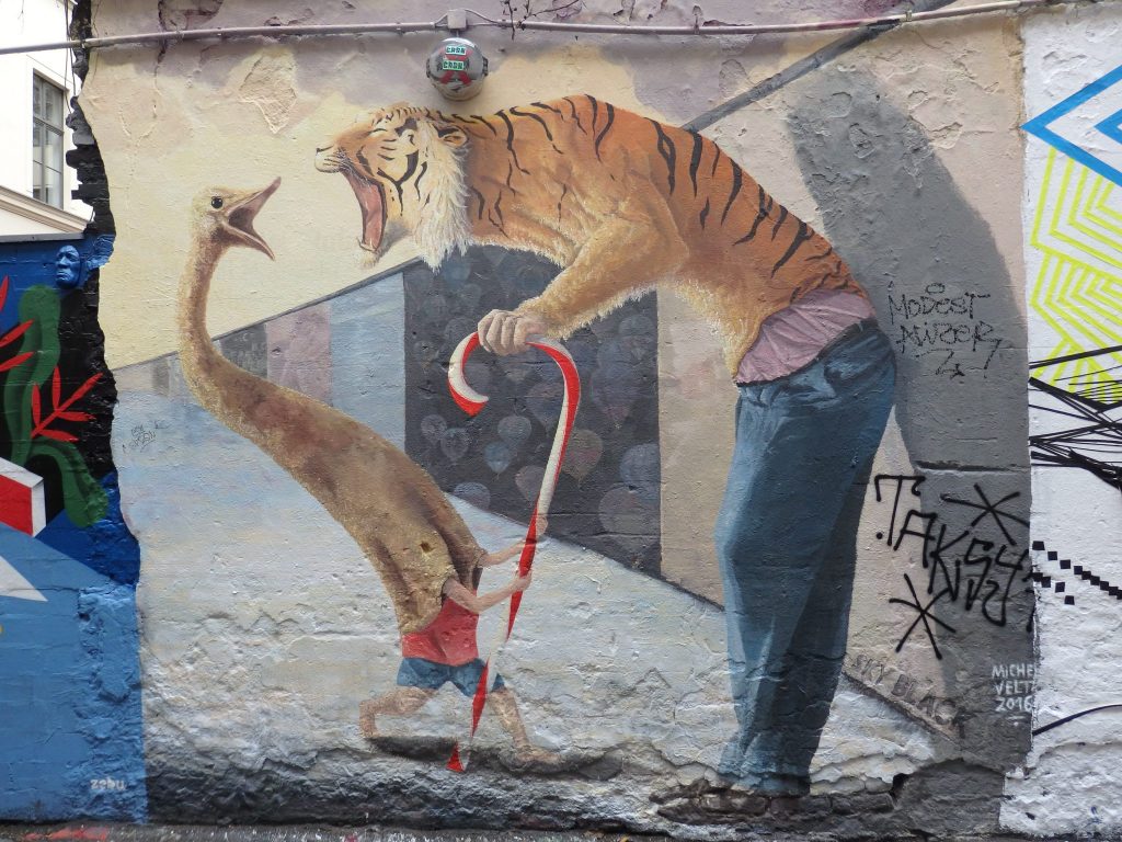 Two figures: left, a goose on its top half but human arms and legs below; right, human legs in jeans but the top half is a tiger. They appear to roar/honk at each other.